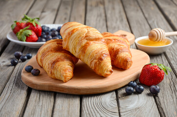 Fresh Croissants with fresh berries on rustic wooden background, selective focus