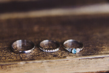 Wedding jewelery closeup. Wedding rings with diamonds and engagement ring with blue jemstone on wooden background. White gold, macro photography.