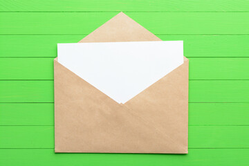 A blank piece of paper with an envelope on green wooden background