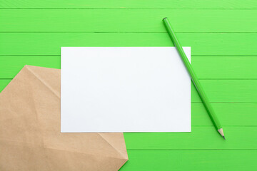 A blank piece of paper with an envelope on green wooden background