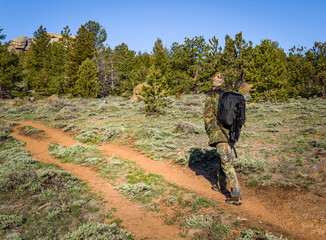A man hiking in camouflage outfit discovering nature in the forest with DSLR photo camera, lenses, tripod in the backpack. Travel photography lifestyle concept.