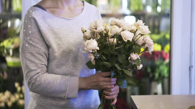 Close up of woman florist s hands arranging white roses in a bunch for sale. Locked down real time close up shot