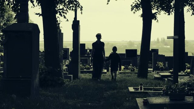 Woman with small boy in cemetery goes straight to camera. Mother and son in graveyard. Two figures in silhouette, central composition, horror horrified atmosphere and color stylization.