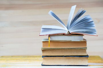 Open book, stack of hardback books on wooden table.