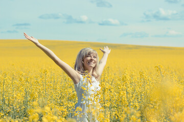 Naklejka na ściany i meble Woman with long hair standing on yellow rapeseed meadow with raised hands. Concept of freedom and happiness.