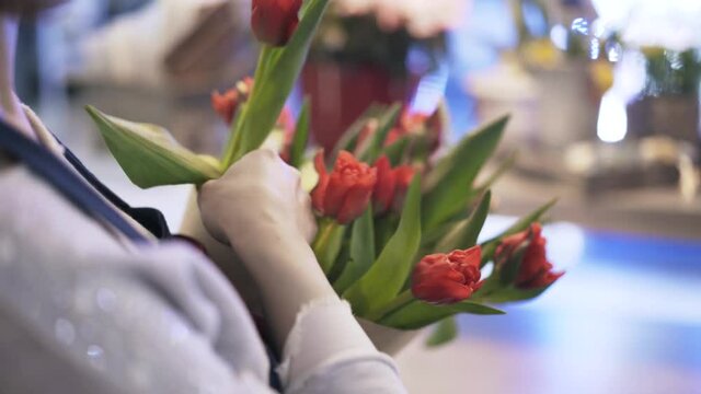 Rear view of a woman florist in casual clothes putting red roses in a conical cardboard box with red threads. Handheld real time close up shot