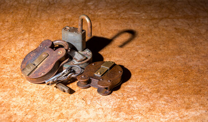 Pile of rusty old padlocks with keys on a brown board background