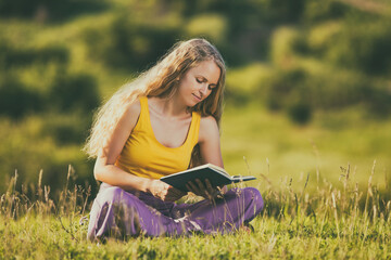 Beautiful woman enjoys reading a book in the nature.