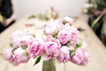 vase of peonies in the foreground. soft focus. Workshop florist, making bouquets and flower arrangements. Woman collecting a bouquet of flowers.