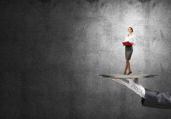 Attractive businesswoman on metal tray with red book in hands against concrete background