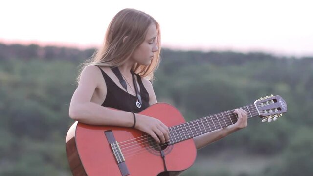 Girl playing acoustic guitar at sunset outdoors