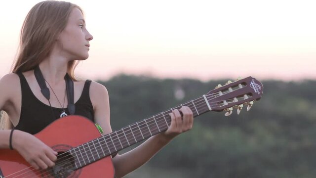 Girl relaxing with the guitar at sunset, panning camera