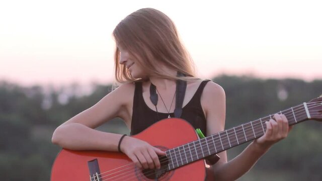 Cute teen girl playing acoustic guitar at sunset