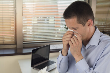 Business man with sneezing in a tissue in an office / workplace. Pollen , ambrosia allergy.