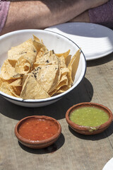 Bowl of tortilla chips with green and red salsa on a table