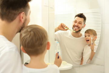Young father with his son brushing teeth and looking in mirror