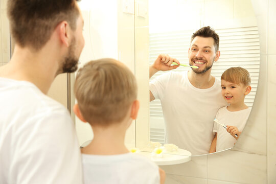 Young father with his son brushing teeth and looking in mirror