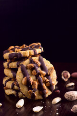 Cookies with peanuts, covered with chocolate icing, on a dark wooden background with space for text.