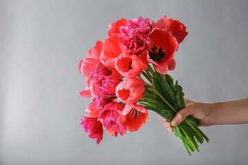 Female hand holding bouquet of fresh tulips on light background