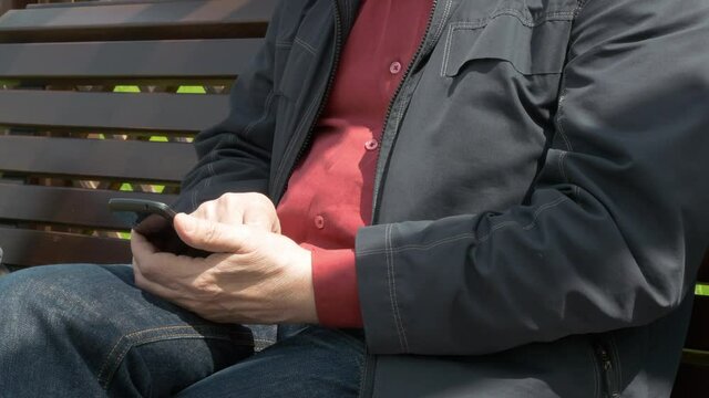 Elderly Man Sitting On Park Bench And Messaging On Mobile Phone
