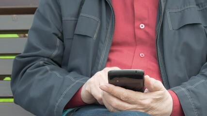 Elderly Man Sitting On Park Bench And Messaging On Mobile Phone