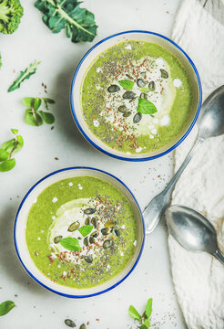 Spring broccoli green cream soup with mint and coconut cream in bowls over light grey marble background, top view. Clean eating, dieting, vegan, vegetarian, healthy food concept