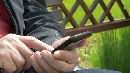 Elderly Man Sitting On Park Bench And Messaging On Mobile Phone