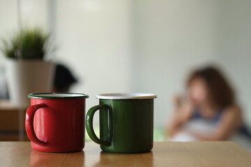 coffee mugs made from metal , green and red color , were placed served on wooden table