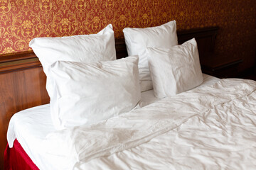 Made bed in the hotel. White pillows with white blanket and red blanket.