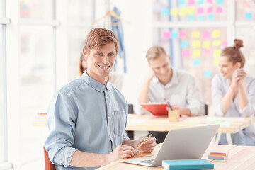 Young man sitting at table and using laptop in office