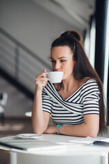 Beautiful young woman holding a cup of coffee looking away and smiling. Cheerful female enjoying a cup of coffee at cafe.