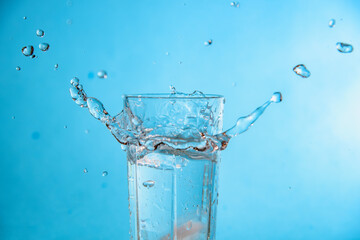Ice dropped in a glass of water, falling in, making a splash and water droplets