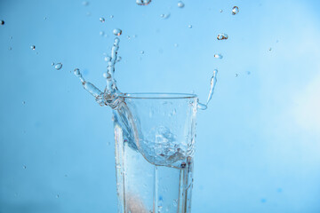 Ice dropped in a glass of water, falling in, making a splash and water droplets