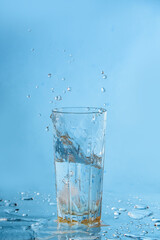 Ice dropped in a glass of water, falling in, making a splash and water droplets