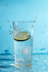 Slice of cucumber dropping into glass of water, making a splash and water drops