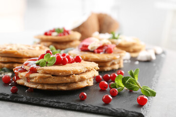 Stacks of delicious coconut pancakes with sweet sauce, berries and mint on slate plate, close up