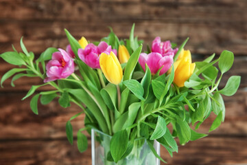 Glass vase with bouquet of beautiful tulips on wooden background