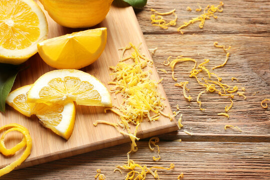 Board with cut lemons and zest on wooden table, closeup
