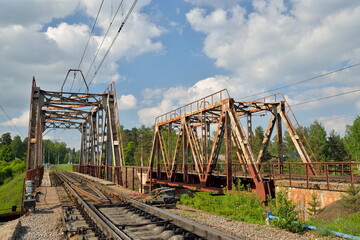 Fototapeta na wymiar Railway bridge across the river and the rails with the arrow in Vyritsa in the summer