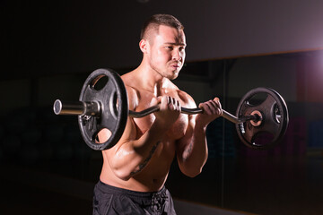 Naklejka na ściany i meble Sporty man doing exercises with barbell on dark background