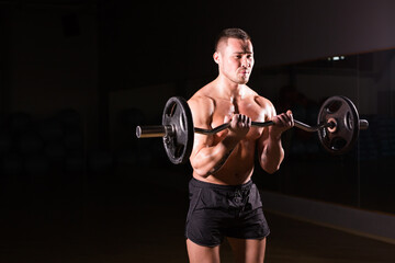 Obraz na płótnie Canvas Sporty man doing exercises with barbell on dark background