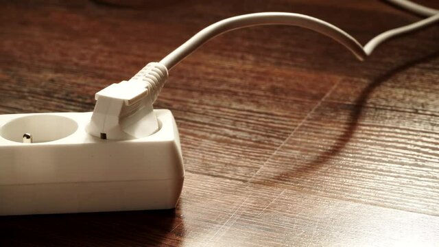 Electricity at home. Close up of white electric plug connected to power strip extension cord on wooden floor. Dolly slider shot 4K ProRes HQ codec