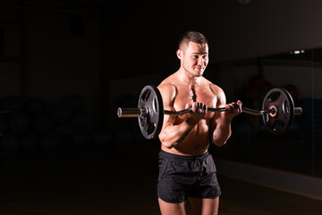 Fototapeta na wymiar Sporty man doing exercises with barbell on dark background