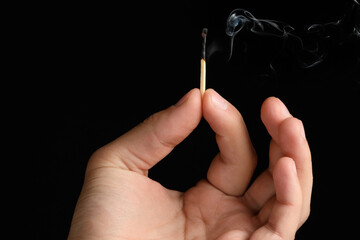 Man's hand holding the extinguished match that blows smoke. isolated on black background