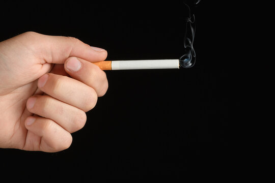 Man's hand holding a smoke cigarette between index finger and thumb in the shape of a gun. isolated on black background
