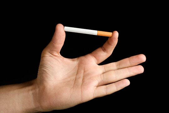 Man's hand holding a cigarette between index finger and thumb. isolated on black background