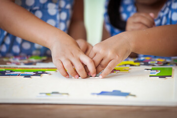 Two children hands helping and trying to connect jigsaw puzzle piece to learn to find solution