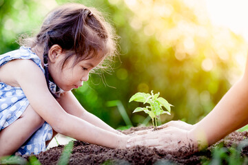 Asian little girl and parent planting young tree on black soil together as save world concept in...