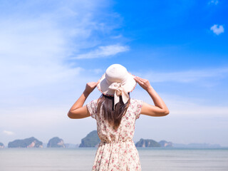 Lonely Woman in summer vacation wearing straw hat and beach dress looking the view at the ocean