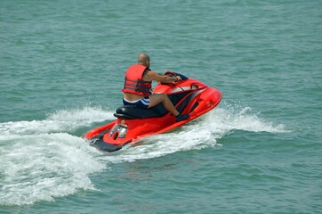 Fototapeta na wymiar A baldheaded man wearing a red life jacket and riding a red jet ski speeding across the florida intra-coastal waterway off Miami Beach.